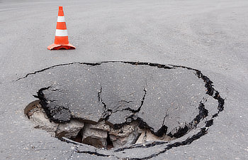 deep sinkhole on street city and orange traffic cone