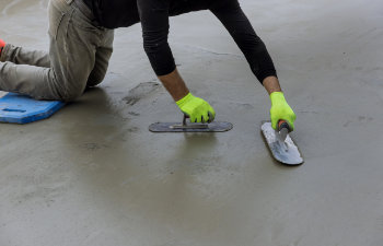 worker holds steel trowel in his hand as he smooths concrete